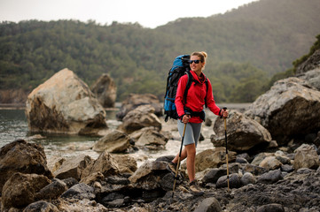 Girl standing on the rocks on the coastline on the sea with hiking backpack