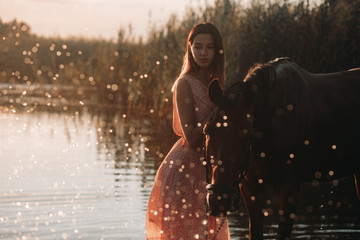 Woman stands next to the horse against background of the river and water splashes.