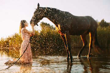 Woman is next to the horse against background of the water splashes at sunset.