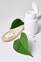 Homeopathy, naturopathy and alternative herbal medicine. Bottle with homeopathic pills on green plant leaf