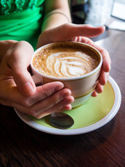 Female hand holding cup of coffee on wooden background