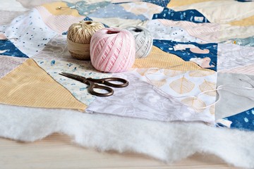 Hand stitch quilting process: cotton thread, needle and scissors on the table