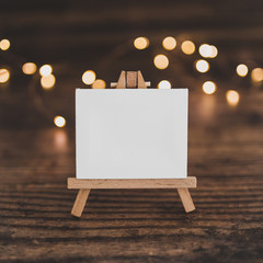 blank canvas miniature surrounded by fairy lights on wooden desk