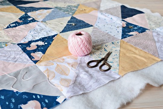 Hand stitch quilting process: pink cotton thread, needle and scissors on the table