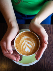 Female hands holding cups of coffee on dark wooden table background, top view.