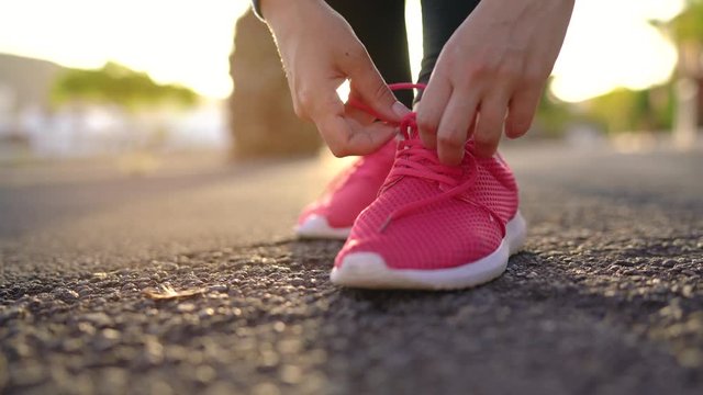 Close up of woman tying shoe laces and running along the palm avenue at sunset
