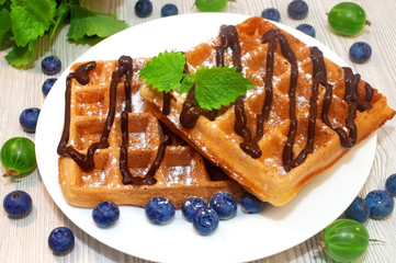 Belgian waffles on a plate with chocolate sauce and blueberries