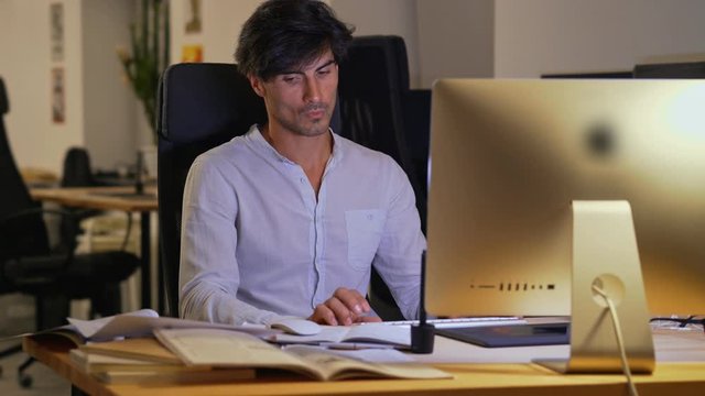Smiling employee man using computer while sitting by the table in office