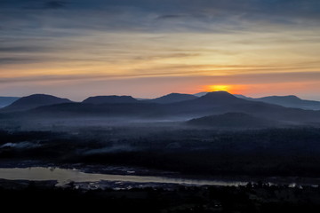 Top view panorama of Mekong river around with soft mist, forest, mountains with cloudy and yellow sun light in the sky background, sunrise at Cha Na Dai Cliff, Ubon Ratchathani, Thailand.