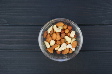 Assorted nuts in a glass bowl on a dark wooden background, top view