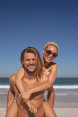 Fototapeta premium Man giving piggyback ride to woman on the beach