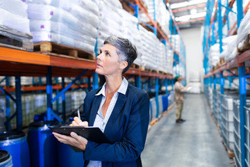 Female manager checking stocks on clipboard in warehouse