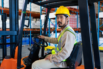 Male worker sitting in forklift and looking at camera in warehouse