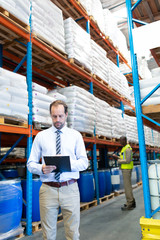 Male supervisor checking stocks on clipboard in warehouse