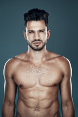 Fototapeta premium Handsome young shirtless man looking at camera while standing against grey background