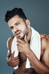 Fototapeta premium Handsome young shirtless man looking at camera while standing against grey background