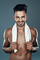 Handsome young shirtless man looking at camera and smiling while standing against grey background