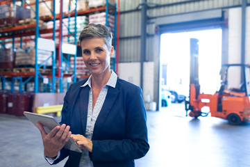 Manager looking at camera while using digital tablet in warehouse