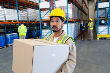 Male worker carrying cardboard box and looking at camera in warehouse