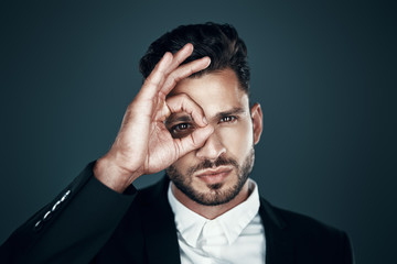 Obraz premium Charming young man in formalwear gesturing and looking at camera while standing against grey background