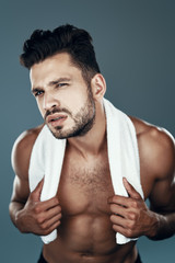 Fototapeta premium Handsome young shirtless man looking at camera while standing against grey background