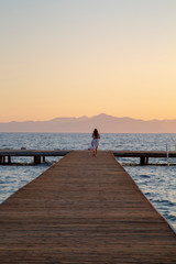 Girl on pontoon pier at sunset . Woman relaxing on pier looking at sea view at sunset