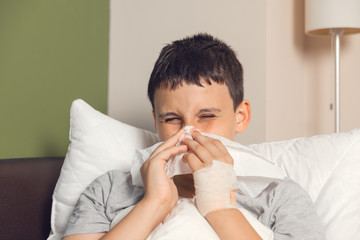 Sick boy laying in a sofa with flu. Nose blowing ill boy.