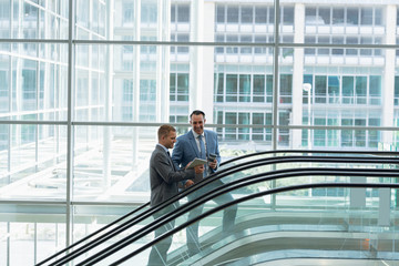 Businessmen interacting with each other while moving upstairs on escalator in office