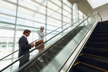 Business people talking on mobile phone and using digital tablet on escalator in a modern office