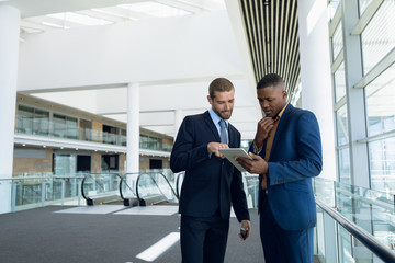 Two businessmen stand using tablet at work