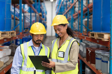 Male and female worker discussing on clipboard in warehouse
