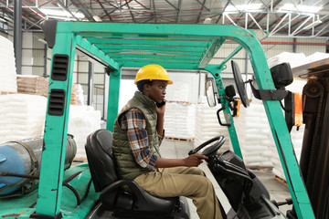Fototapeta na wymiar Female worker talking on mobile phone while driving forklift in warehouse