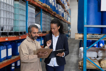 Female manager and male worker discussing over clipboard in warehouse