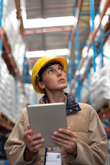 Female worker with digital tablet looking up in warehouse