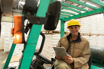Female worker using digital tablet while sitting in forklift in warehouse