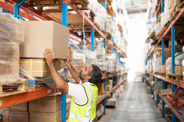Male worker putting cardboard box on a rack in warehouse