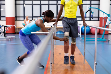 Physiotherapist assisting disabled man walk with parallel bars in sports center