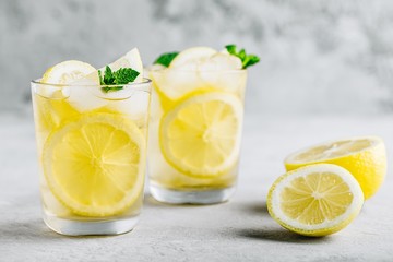 Lemonade with lemon, mint and ice cubes in glass on gray stone background. - obrazy, fototapety, plakaty
