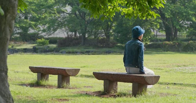 Woman sit on the wooden bench and look around in the park