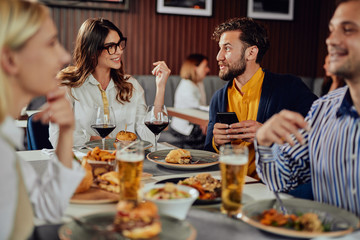 Multiethnic friends sitting at restaurant, drinking alcohol, chatting and having burgers for dinner.