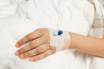 Cannula inserted in sick kid on white duvet.