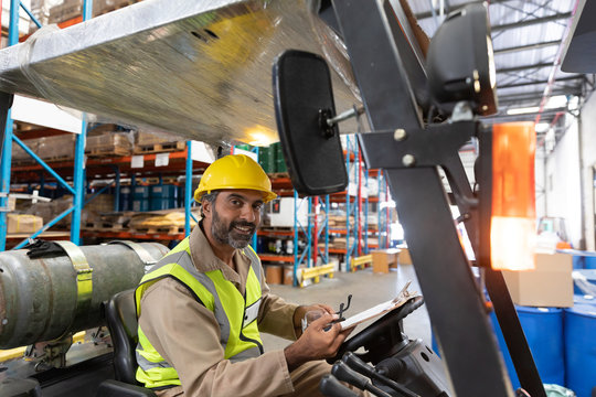 Male staff looking at camera while sitting on forklift in warehouse