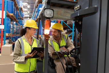 Male and female staff discussing over clipboard in warehouse