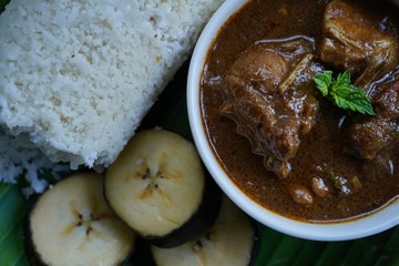 Popular South Indian breakfast steamed rice Puttu with Chicken curry served in banana leaf, selective focus