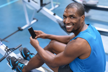 Fit man using mobile phone while exercising on rowing machine in fitness center