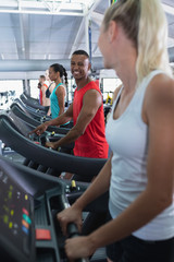 Fit man interacting with woman while exercising on treadmill