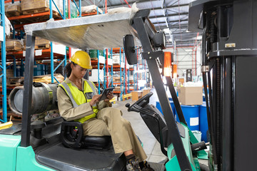 Female staff using digital tablet while sitting on forklift