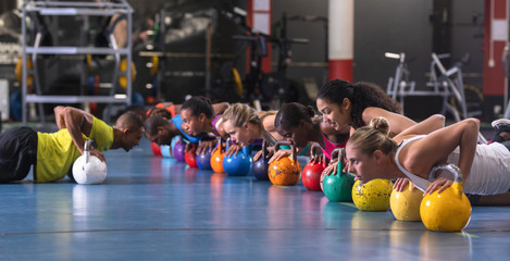 Male trainer training women to perform exercise with kettlebell - Powered by Adobe