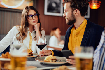 Two Caucasian friends dressed smart casual having dinner and chatting while sitting in restautrant.