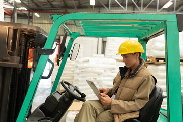 Female worker using digital tablet while sitting in forklift in warehouse